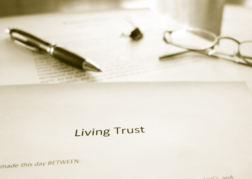 A paper that says Living Trust on top of other documents with a pen and glasses laying on the paper 