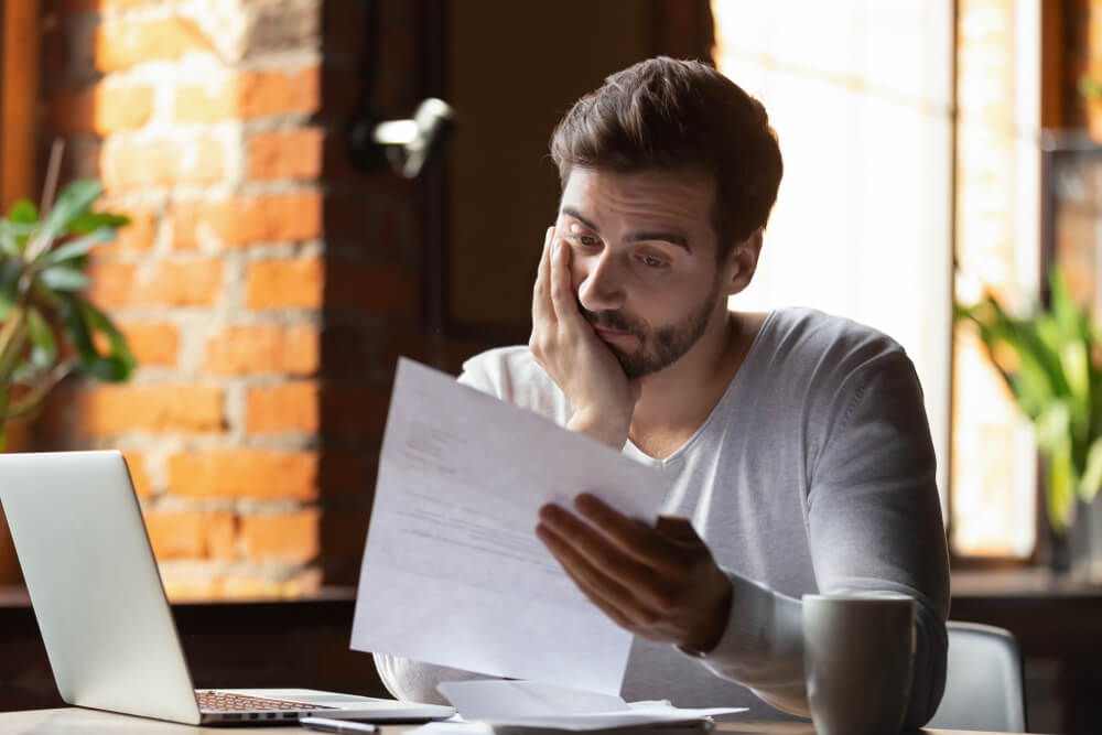 Man sitting at his desk looking at a paper confused and frustrated with one hand on his fasce