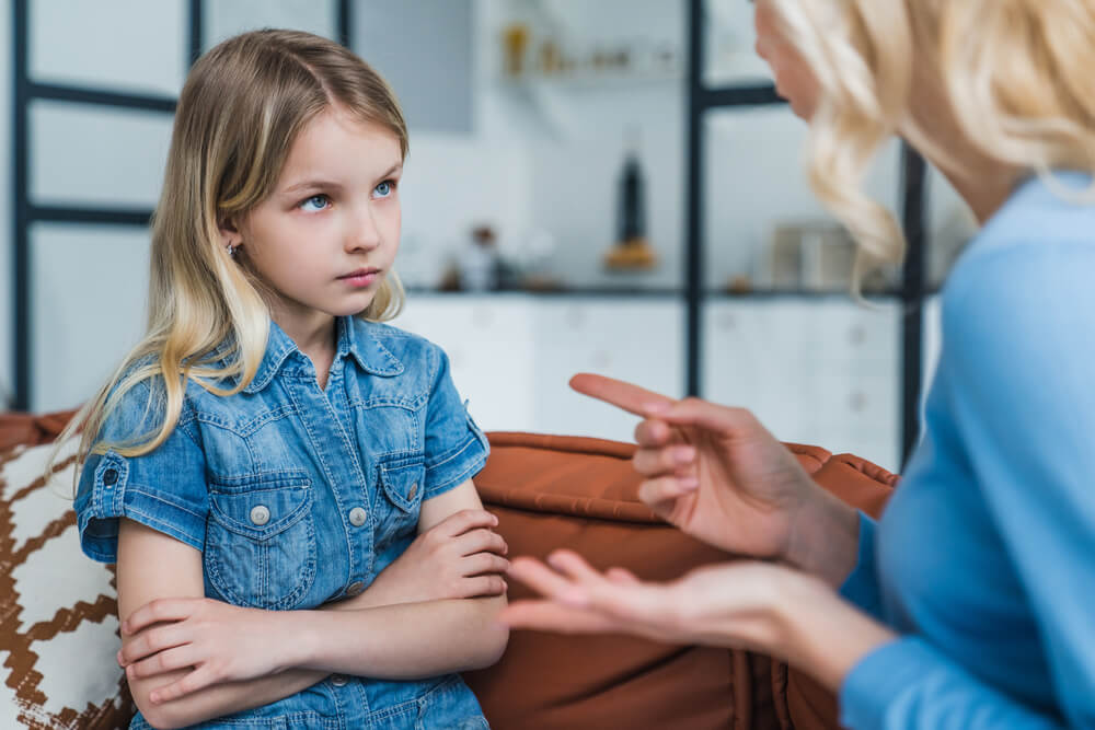 Little girl who looks sad is sitting down while her mother talks to her, the mother is pointing at the daughter