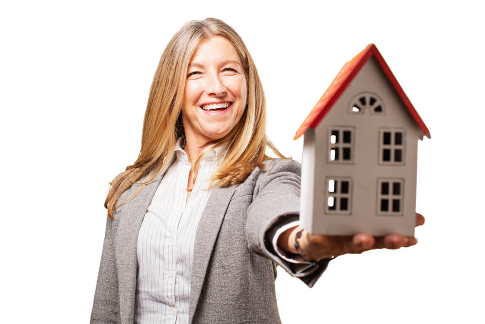 A smiling women holding a toy house on one of her hands and her arm is extended away from her body