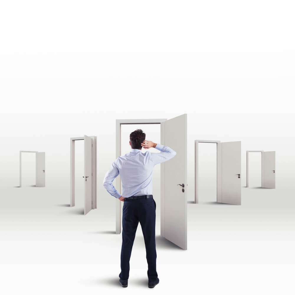 A man standing in front of five different white doors that are open, the man has his left hand on his hip and his right hand on his forehead