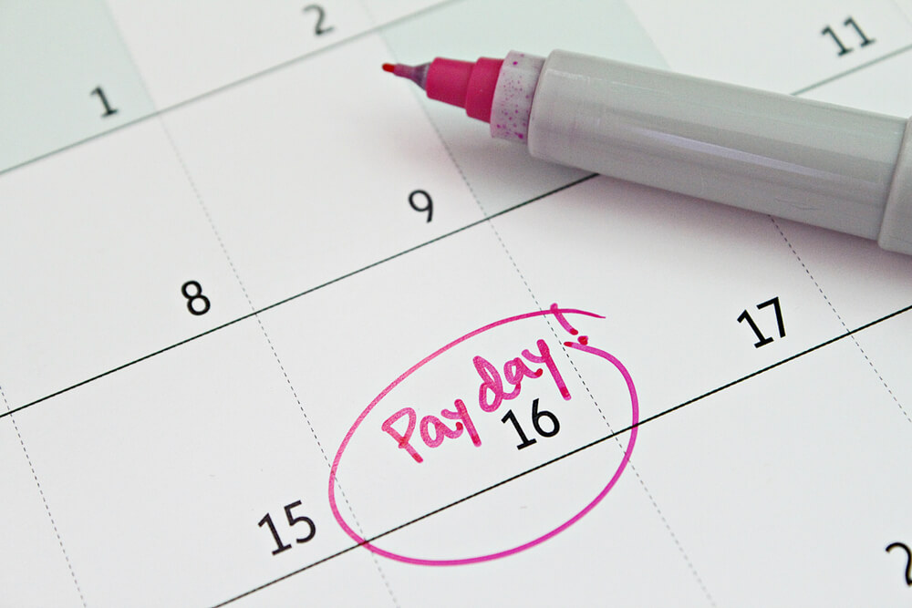 A close up of an empty calendar that only says pay day in pink on the 16th and it is circled 