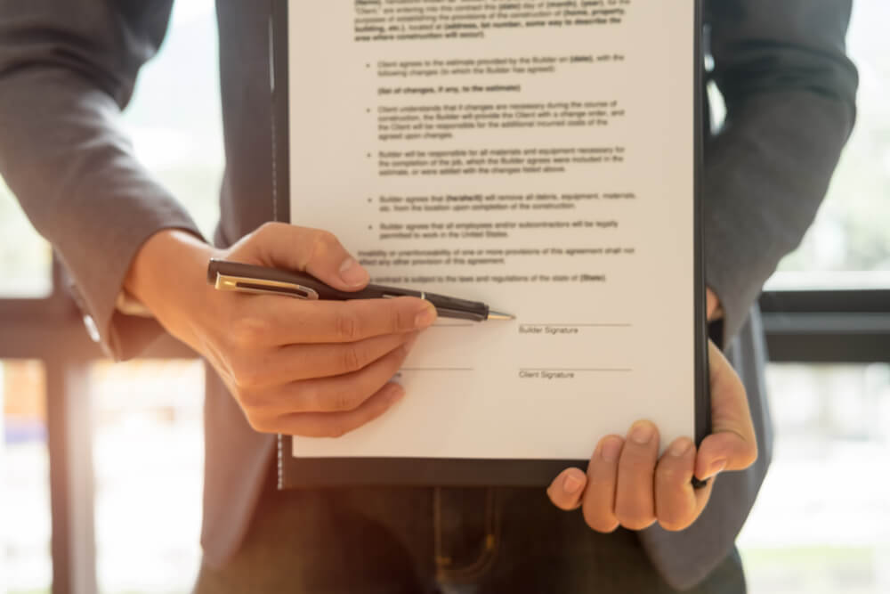 A man holding papers up in one hand in a pen in the other, he is using the pen to point where the document needs to be signed 