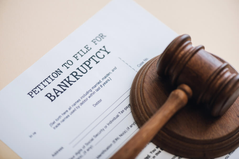 A petition for bankruptcy paper sitting on a tan desk with a sound block and gavel rest on top of the paper