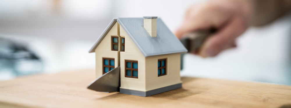 A little toy house being cut in half by a person holding a kitchen knife 