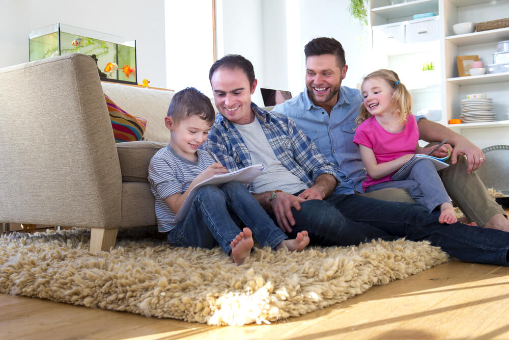 Two married men sitting on the ground with their son and daughter 