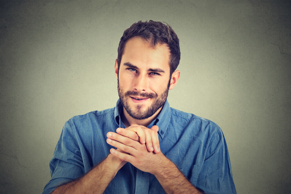 A scheming man holding both of his hands up rubbing them together