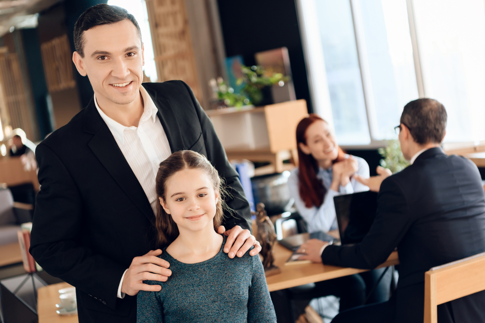 Joyful adult man is standing in foreground and hugging joyful girl in lawyer's office. Family in office of family lawyer.