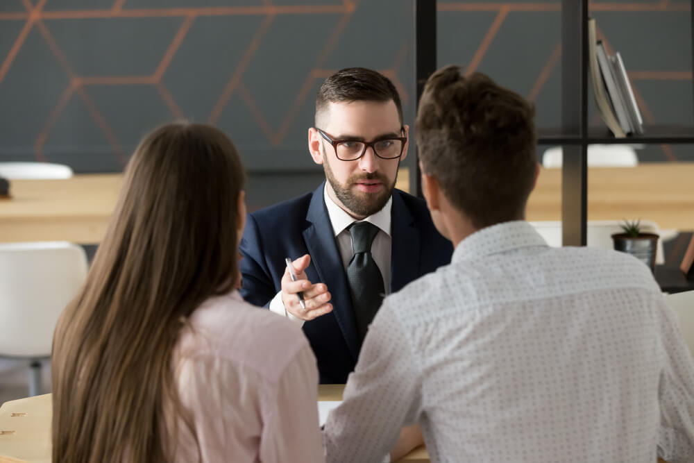 A couple sitting at a table facing a businessman who is explaining something to the couple