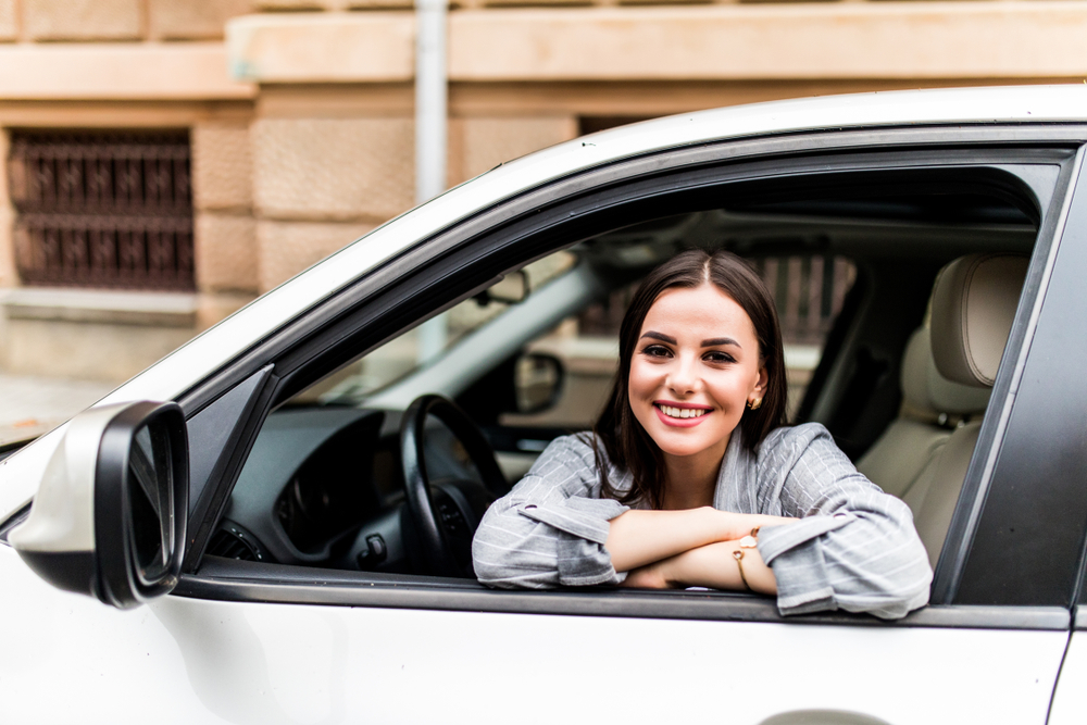 Closeup portrait attractive woman buyer sitting in her new car excited ready for trip isolated outside dealer dealership lot office. Personal transportation auto purchase concept