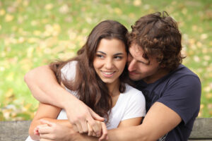 Pretty couple hugging and flirting in an urban park sitting in a bench and looking away