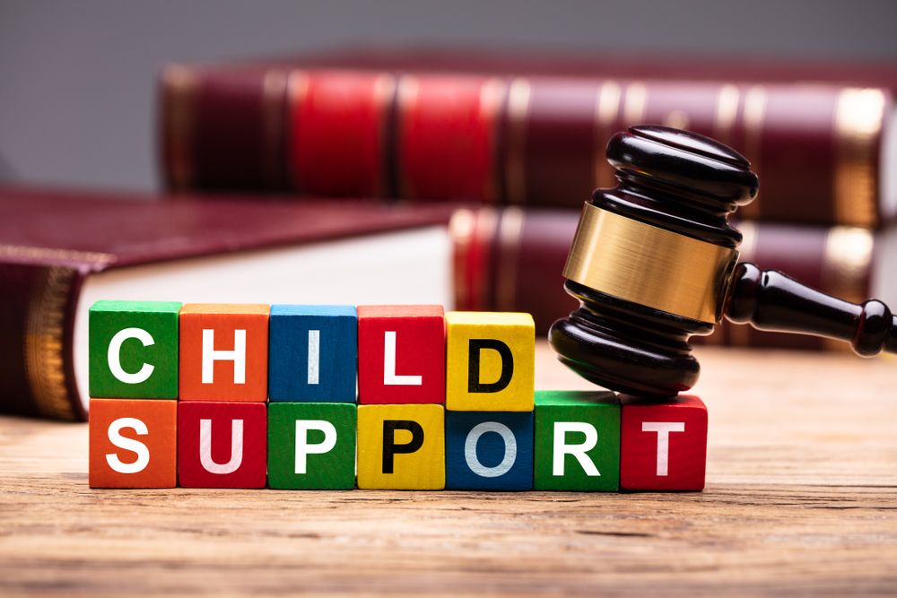 A judge's gavel rests next to colorful blocks spelling "CHILD SUPPORT," with law books in the background.