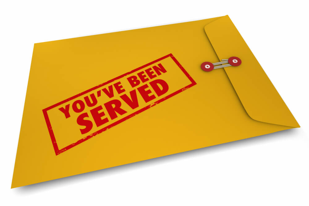 An image of a manila envelope sitting on a white surface with a red stamp on it saying you've been served 