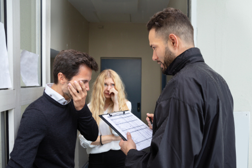 Bailiff Talking With Sad Couple At Home Entrance