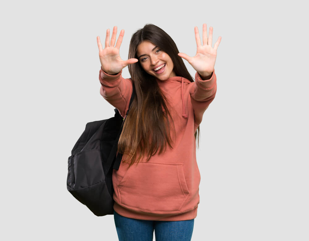 A girl standing against a white background holding up ten fingers 