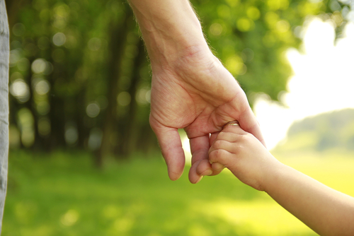 An unmarried father in Texas gently holds his child's hand, as they walk together amidst lush green foliage, embodying the cherished bond and shared rights they treasure.