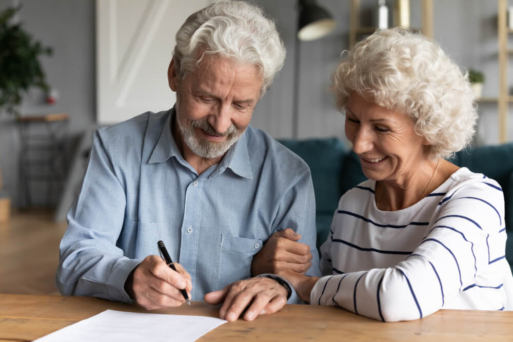 A picture of an older couple sitting at a desk signing documents