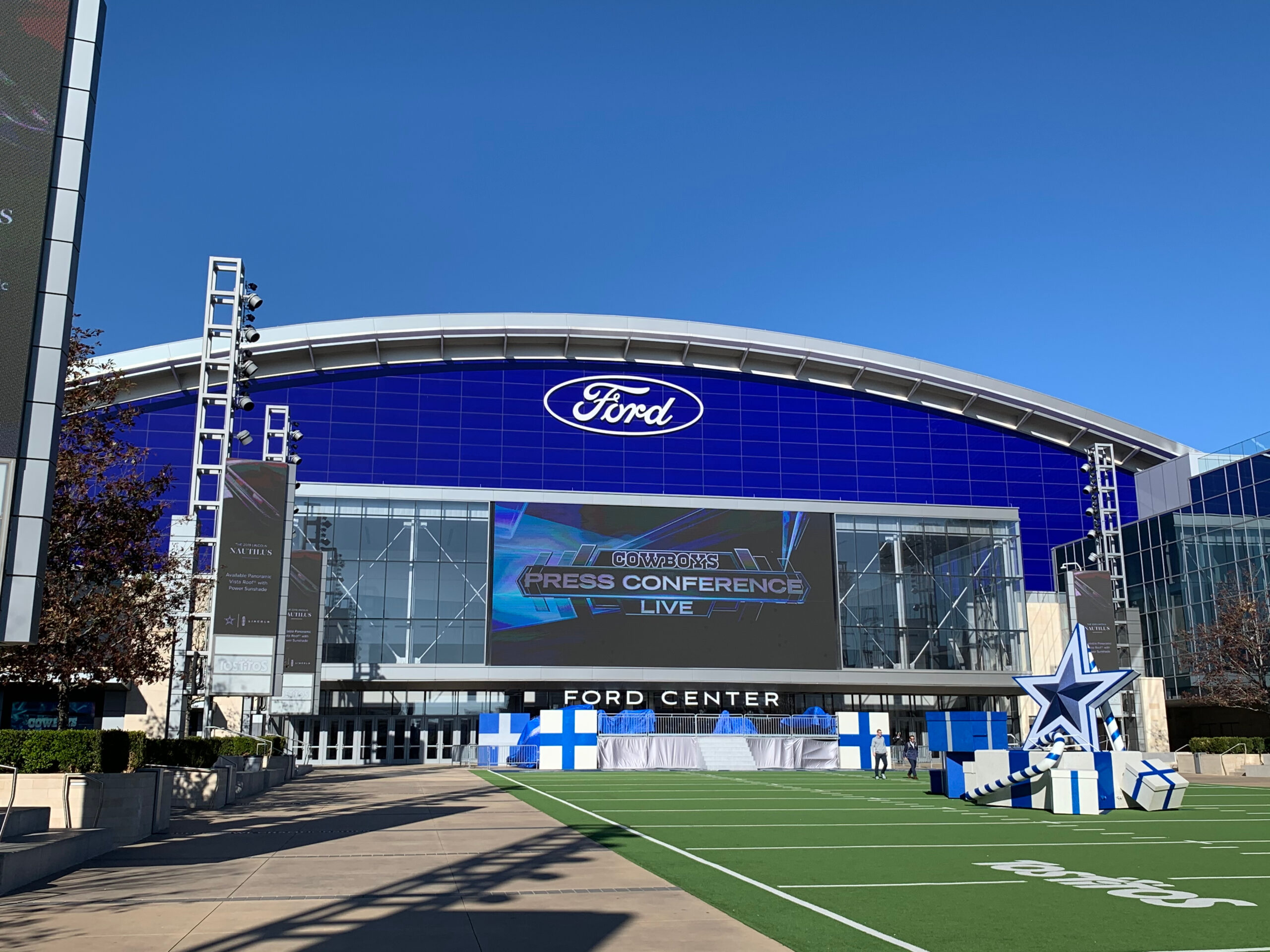 Exterior of the Ford Center, featuring a large glass facade with Ford branding, adjacent to a football-themed plaza under a clear blue sky, near top-rated divorce lawyers in Frisco.