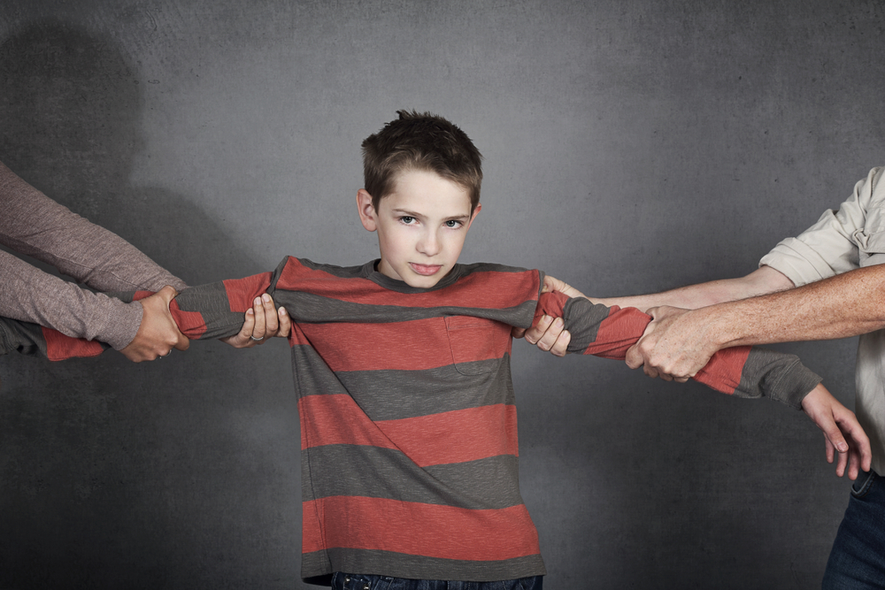 teenager boy undergoing divorce from his parents on gray studio background