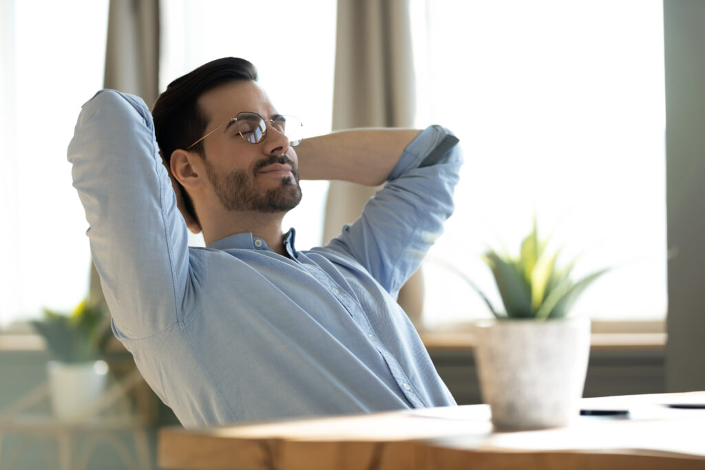 Man relaxing with hands behind head at a desk, appearing content and thoughtful.