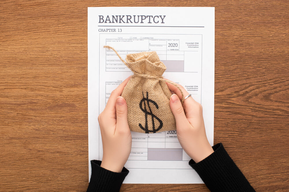 A chapter 13 bankruptcy paper sitting on a wooden table with a person holding a bag with the money symbol over the papers 