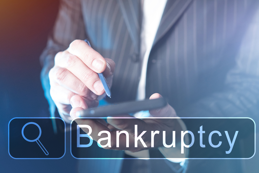 A person in a business suit uses a digital tablet with the word "Bankruptcy" and a search icon superimposed, highlighting concerns like how much does it cost a creditor to sue you.