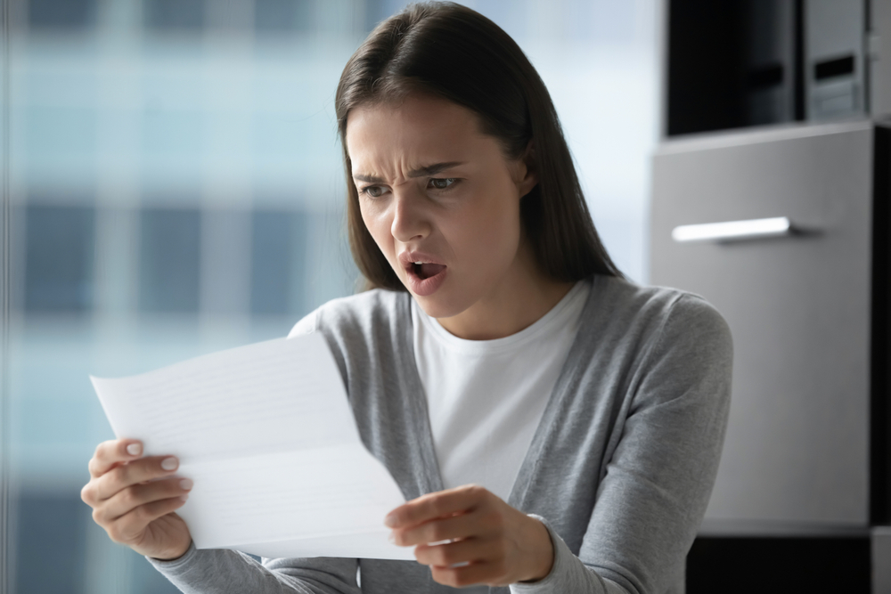 Angry annoyed young businesswoman employee reading letter, working with correspondence, frustrated stressed woman received bad news, holding document, dismissal or debt notification