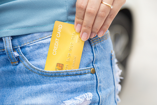 A hand slides a yellow credit card into the front pocket of blue jeans, perhaps wondering if there's a way to exclude such cards from Chapter 7 considerations.