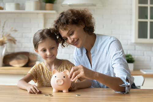 A woman and child sit at a table, placing coins into a piggy bank, as if the custodial parent makes more money.