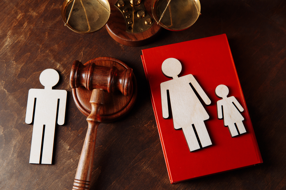 Wooden figures of a man, woman, and child, a gavel, scales of justice, and a red book on a wooden table, symbolizing family law or custody issues such as standard possession order Texas Mother's Day rights.