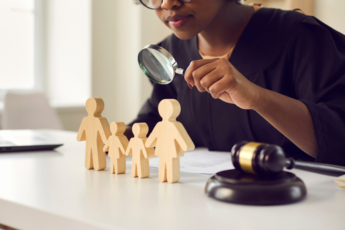 Black judge or lawyer looking in magnifying glass at little mom, dad children figures on desk. Family law court case investigation, divorce, joint custody of kid, parental rights deprivation concept, can permanent custody be overturned