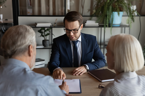 Confident lawyer, real estate agent, financial advisor giving consultation to mature couple of clients, explaining legal documents, helping to paper form, contract, agreement for signing.
