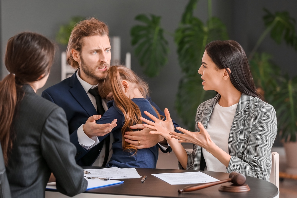 A man and woman are having a serious discussion at a table with a female official present; the man holds an upset young girl. Legal documents and a gavel suggest a possible texas unfit parent case is being addressed.