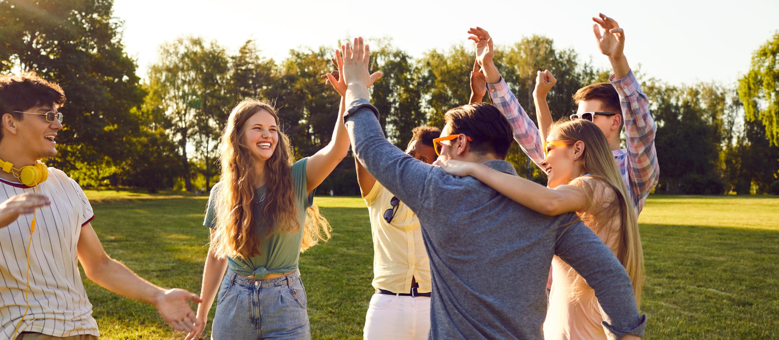 Group of six young friends in a park hugging and high fiving