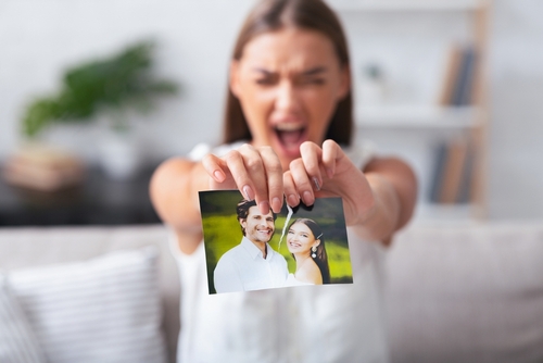 Breakup. Furious Woman Ripping Wedding Photo With Ex-Husband Sitting On Sofa Indoor After Divorce. Selective Focus