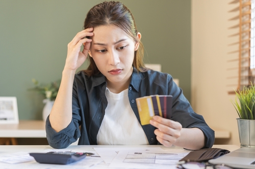 Financial owe, hand of asian woman sitting, holding credit card, stressed  by calculate expense from invoice or bill, no money to pay, mortgage or loan. Debt, bankruptcy or bankrupt