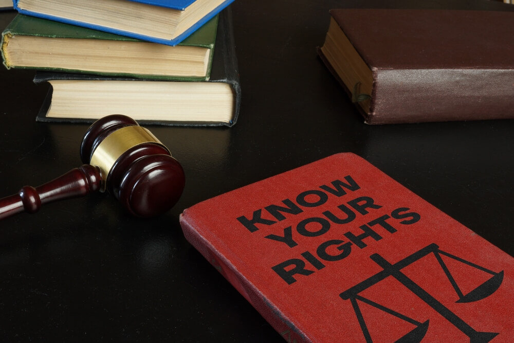 A red book that says know your rights with the scale of justice on it sitting next to a judges gavel and other stacked books