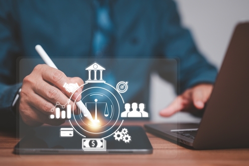 A person in a blue shirt uses a stylus on a laptop, with digital business icons like graphs, scales, and gears overlayed, pondering how assets held overseas are treated in a divorce.