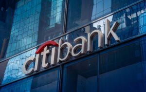 Citibank logo on the exterior of a glass building with reflections of other buildings, including Morgan and Associates, on the sleek glass surface.
