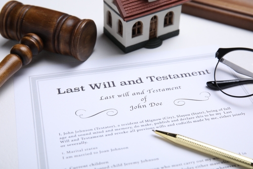 Close-up of a will-based estate plan document alongside a gavel, model house, eyeglasses, and pen on a white surface.