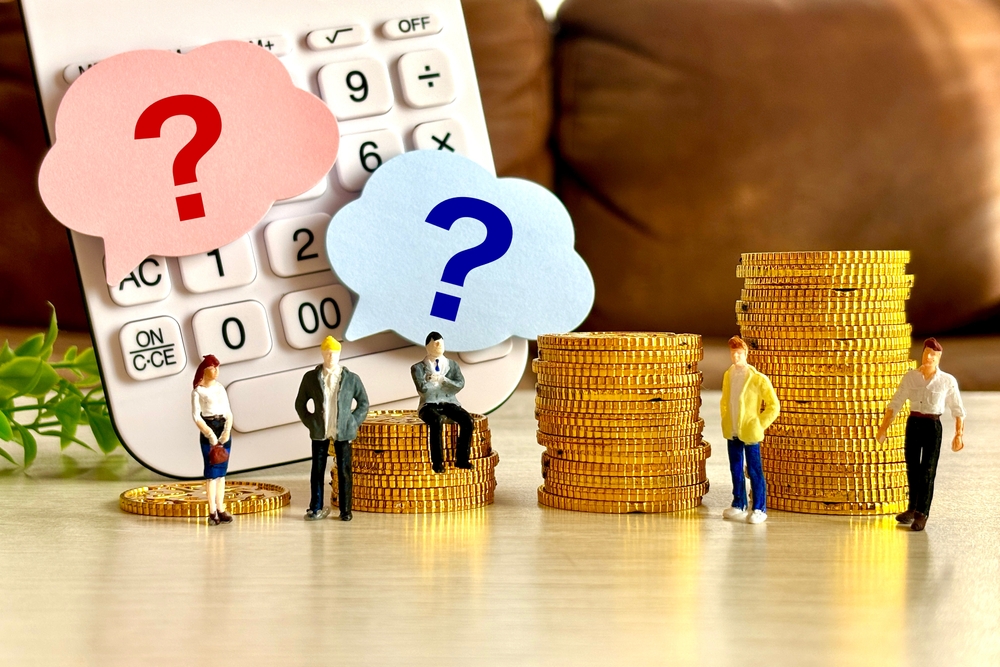 Miniature business people stand on stacks of gold coins in front of a calculator with question marks, symbolizing financial planning and questions about wealth and net worth