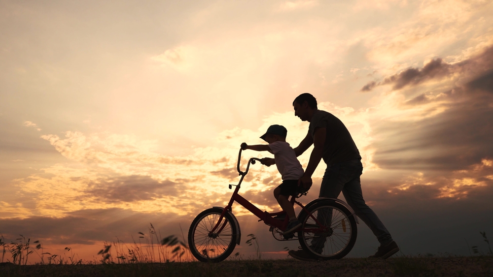happy family in the park. father teaching son to ride a bike at sunset silhouette in the park, illustrating how to win a child support modification case