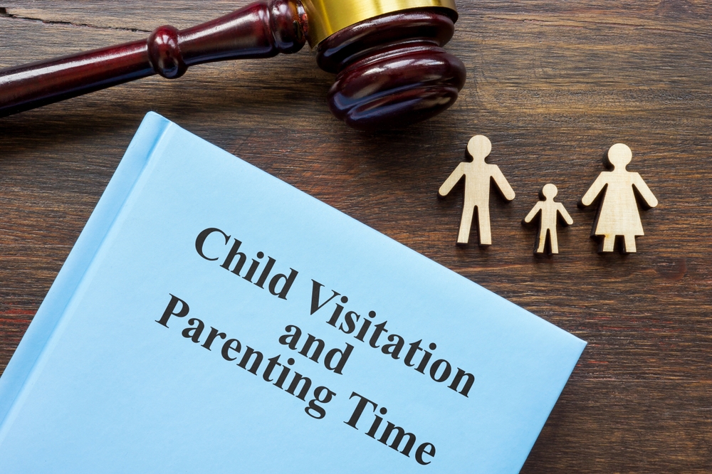 A gavel, wooden family figures, and a blue book titled "Child Visitation and Parenting Time" on a wooden table