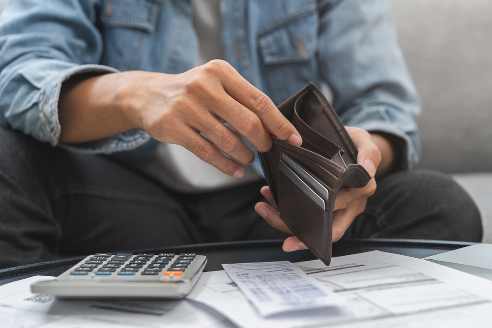 A person holds an open wallet with credit cards, sitting at a table with a calculator and bills.