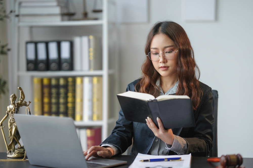 Lawyer is checking a law book and typing on a laptop while working at her desk