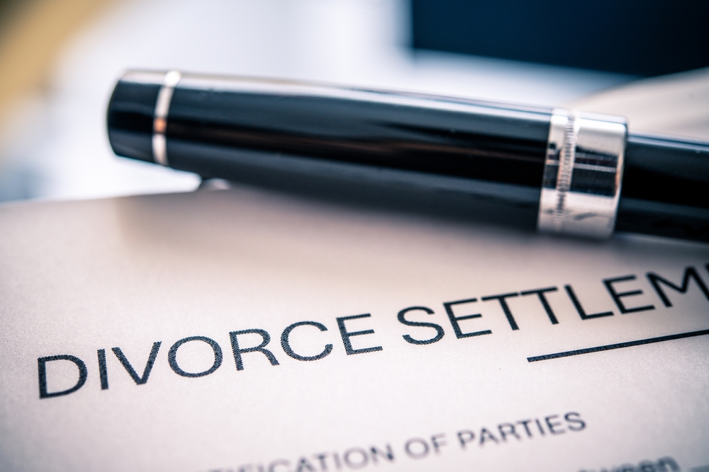 A divorce settlement agreement prominently displayed with a sleek black pen serving as a tool for signing legal documents related to marital separation and financial resolutions.