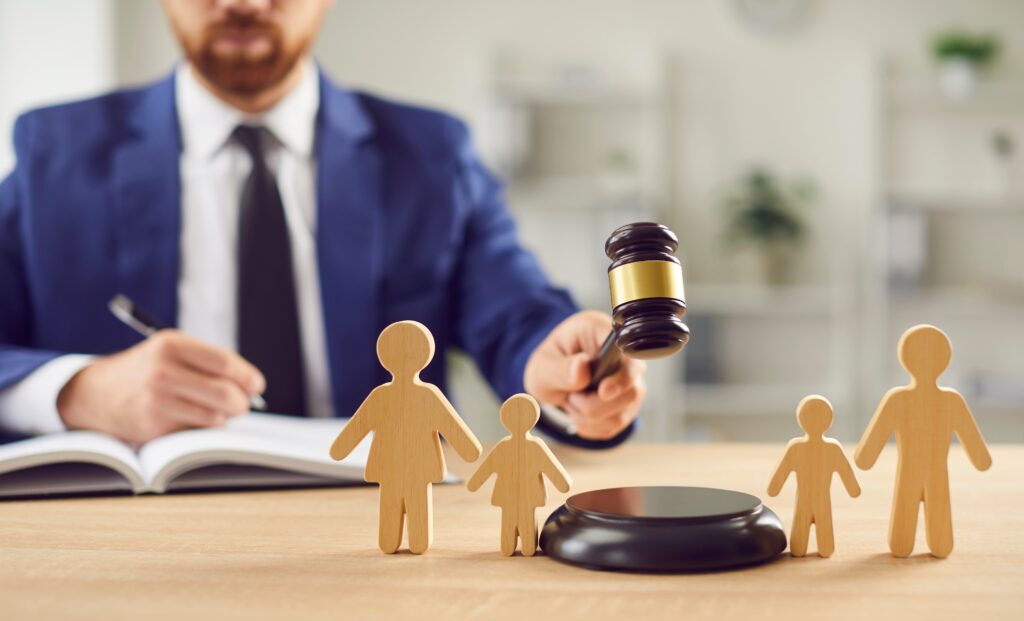 A person in a suit uses a gavel near wooden family figures on a table.