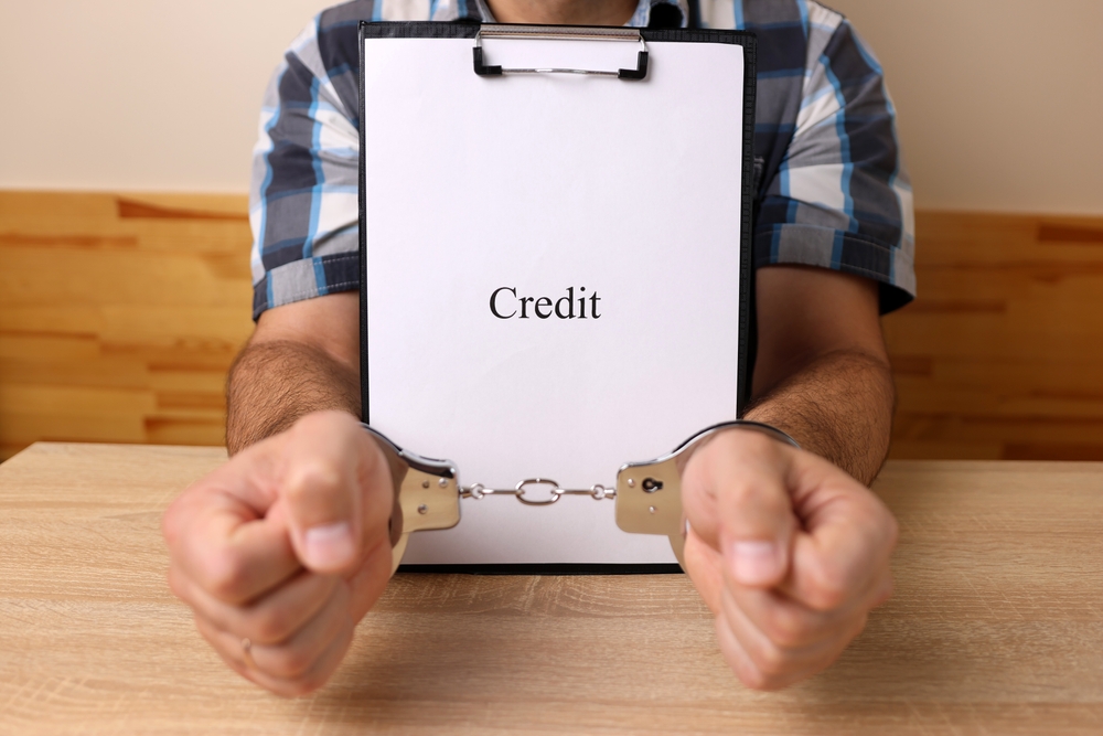 A man in handcuffs holding a document with the word credit. The concept of dependence on credit.