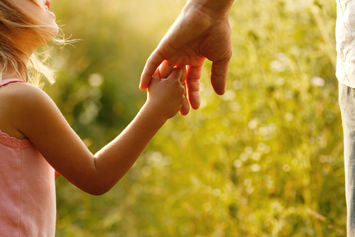 Amidst a grassy field, sunlight illuminates a child holding an adult's hand, resembling the poignant moments often witnessed during custody discussions in Texas divorce proceedings.