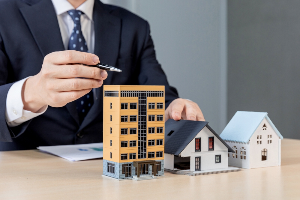 A person in a suit points with a pen at miniature models of residential buildings on a desk